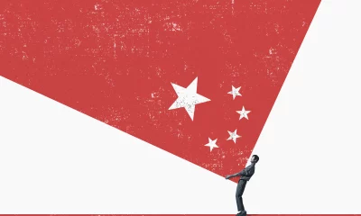 Figura humana em preto e branco segura uma superfície triangular branca contra um fundo vermelho com estrelas, remetendo à bandeira da China.