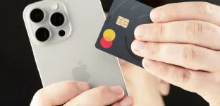 Mãos segurando um iPhone prateado e um cartão Mastercard de design escuro e minimalista.