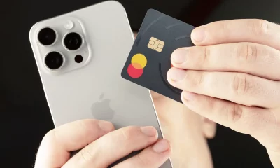 Mãos segurando um iPhone prateado e um cartão Mastercard de design escuro e minimalista.