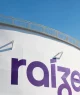 Tanque industrial branco com logotipo "raizen" em roxo, escada lateral e céu azul claro ao fundo.