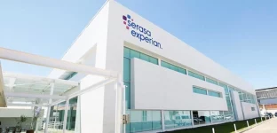 Fachada de prédio com letreiro da empresa Serasa Experian. O prédio tem acabamento em alvenaria branca e vidros azuis espelhados. A imagem tem uma perspectiva forçada, onde se vê a frente a lateral esquerda da edificação.