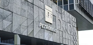 Fachada de um edifício moderno e geométrico da Petrobras, com logotipo "BR" e nome destacado, cercado por uma cerca metálica cinza.