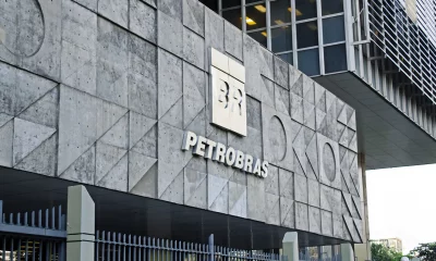 Fachada de um edifício moderno e geométrico da Petrobras, com logotipo "BR" e nome destacado, cercado por uma cerca metálica cinza.