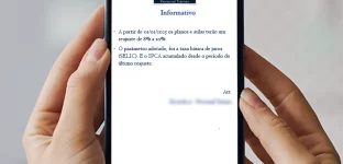 Um smartphone está sendo segurado por uma mão, exibindo um comunicado de reajuste de preços da RJ Personal Trainer na tela.