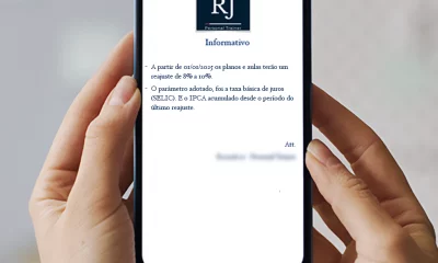 Um smartphone está sendo segurado por uma mão, exibindo um comunicado de reajuste de preços da RJ Personal Trainer na tela.