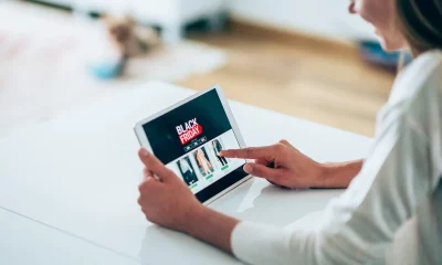 Uma pessoa navegando em uma página de compras online de Black Friday em um tablet sobre uma superfície branca, em um ambiente residencial iluminado.