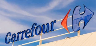 Logomarca do Carrefour destacada em um letreiro elevado contra um céu parcialmente nublado.