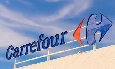 Logomarca do Carrefour destacada em um letreiro elevado contra um céu parcialmente nublado.