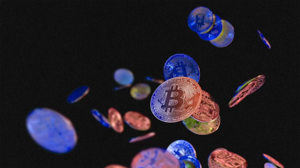 Moedas virtuais flutuam contra um fundo preto, com um Bitcoin destacado no centro, rodeado por tons metálicos de azul, vermelho e dourado.