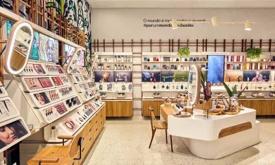 Imagem de uma loja da Natura, marca de cosméticos, moderna e bem iluminada com prateleiras cheias de produtos de maquiagem, perfumes e cosméticos para homens, e uma ilha central com design sofisticado.