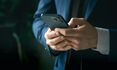 Em um ambiente interno suavemente iluminado, uma pessoa em um terno azul escuro segura um celular moderno com múltiplas lentes.