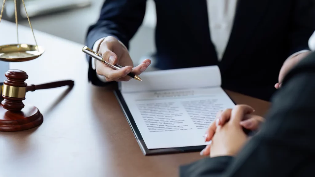 Duas pessoas em uma reunião profissional com documentos e símbolos jurídicos ao fundo.